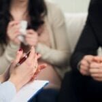 Couple attending a therapy session with a counselor taking notes.
