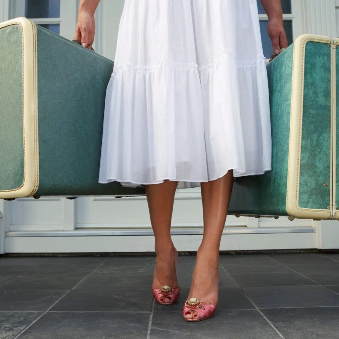 Person in a white dress holding two green suitcases, wearing pink heels. Person in a white dress holding two green suitcases, wearing pink heels.